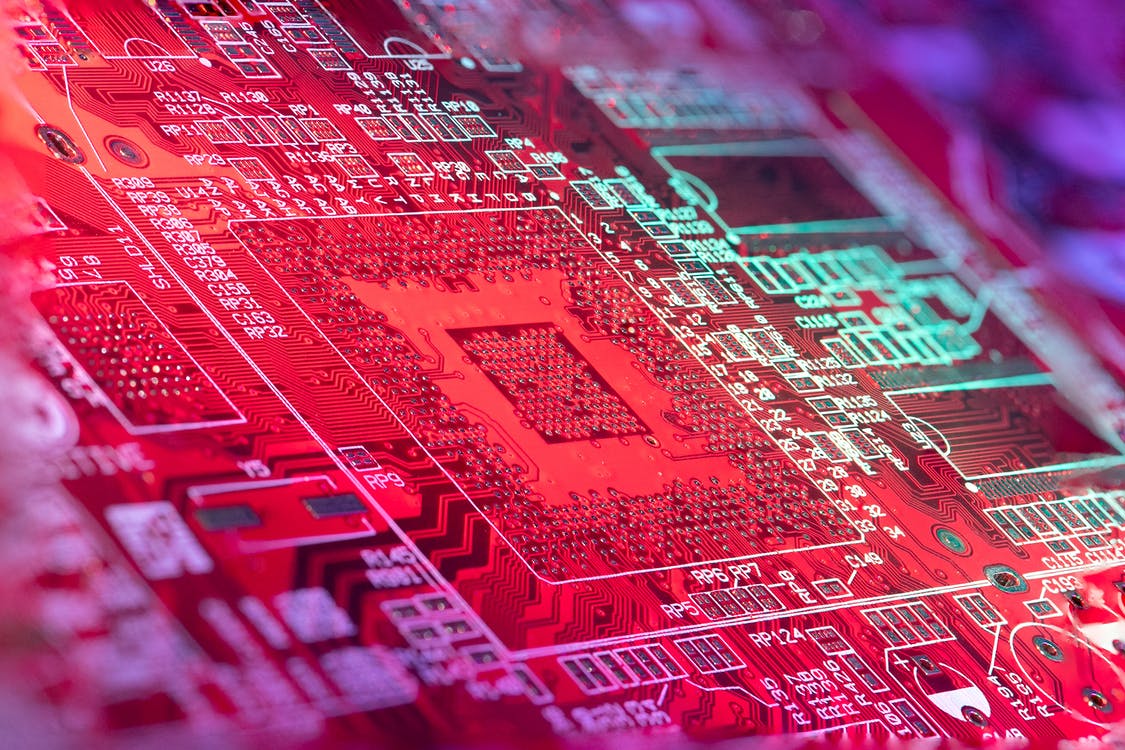 Red printed board of digital device with bright electric circuit with numbers and symbols placed in room on blurred background