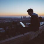 A person sitting on a ledge with a computer Description automatically generated with low confidence