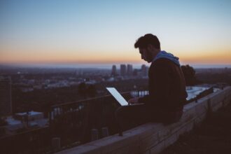 A person sitting on a ledge with a computer Description automatically generated with low confidence