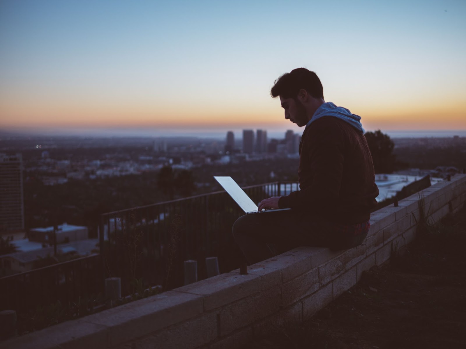 A person sitting on a ledge with a computer Description automatically generated with low confidence